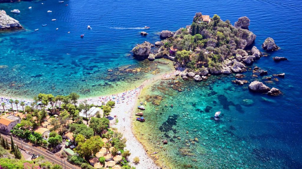 Sun-kissed Taormina Beach in Sicily, Italy, with golden sands, turquoise waters, and the silhouette of the historic Taormina town.