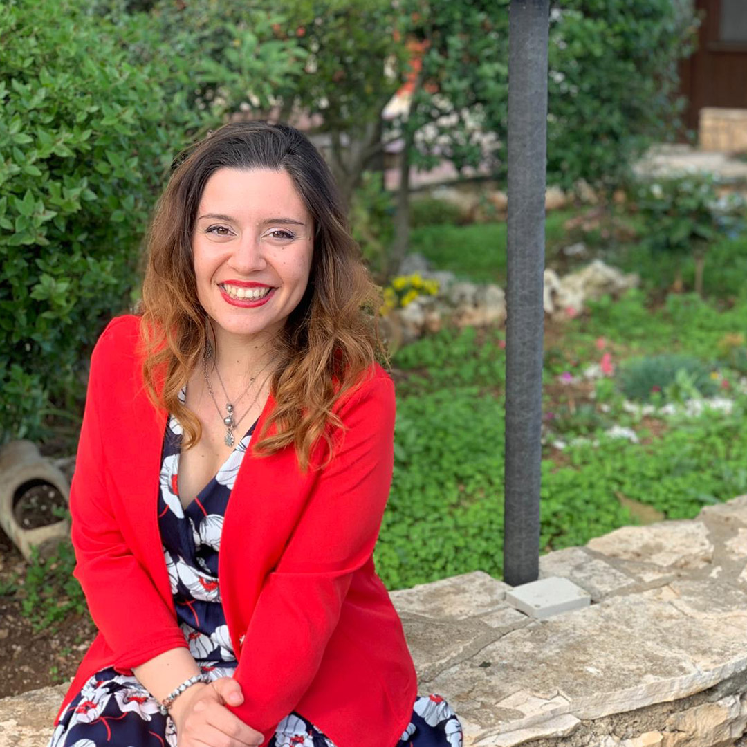 A woman in a red jacket sitting on a stone wall.