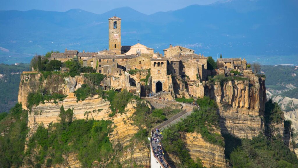 Enchanting view of Civita di Bagnoregio in Umbria, Italy, a historic hilltop town surrounded by lush greenery and connected by a charming stone bridge.