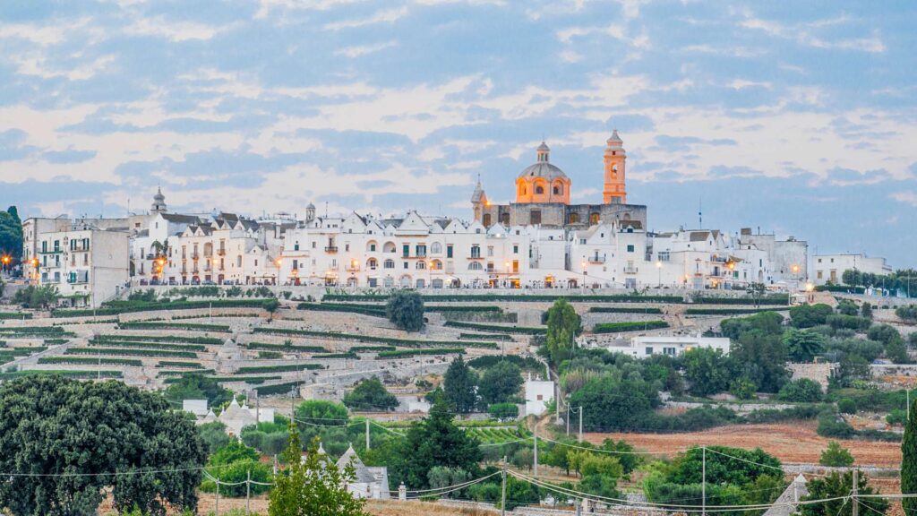 Dusk view of Locorotondo in Puglia, Italy, showcasing the charming architecture and warm glow of lights against the evening sky.