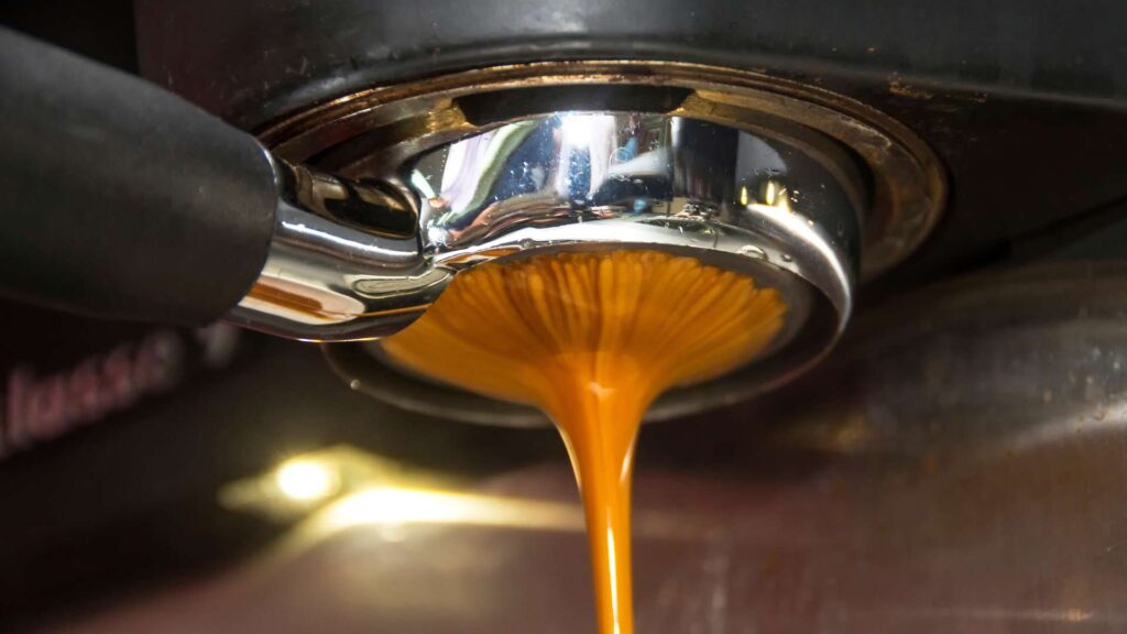 An espresso machine in action, with rich, dark espresso pouring into a small cup below