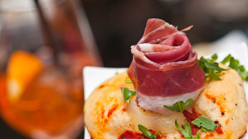 A small Italian pizzetta topped with thin slices of prosciutto crudo, fresh arugula, and shavings of mozzarella cheese