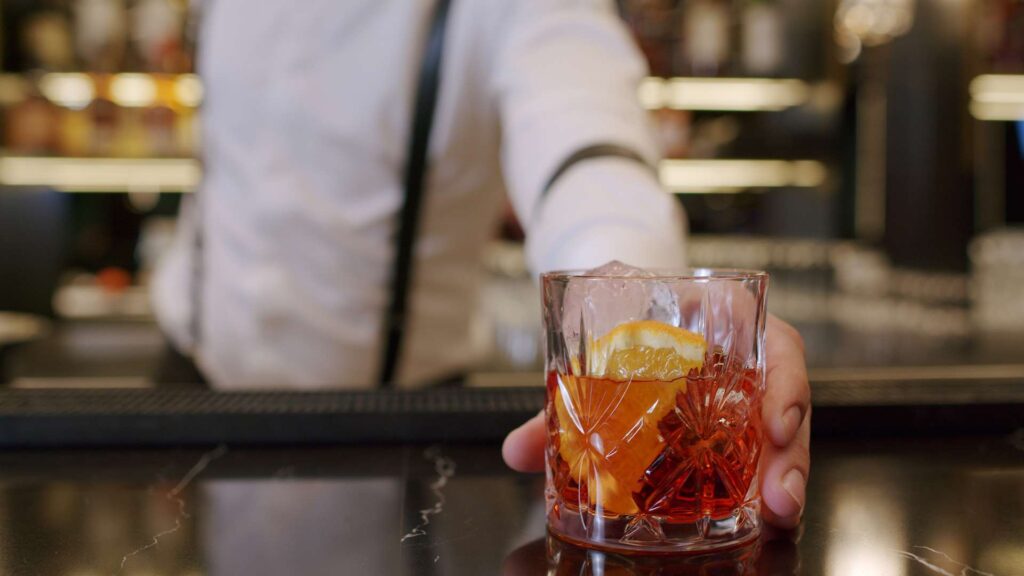 A classic Italian Negroni cocktail served in a crystal glass, garnished with a twist of orange peel and surrounded by ice cubes.