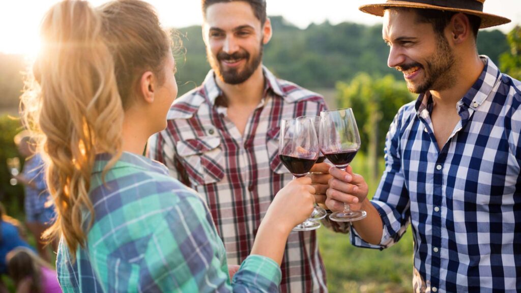 A group of people enjoying a wine tasting experience in an Italian vineyard, surrounded by lush green vine rows and scenic countryside views.