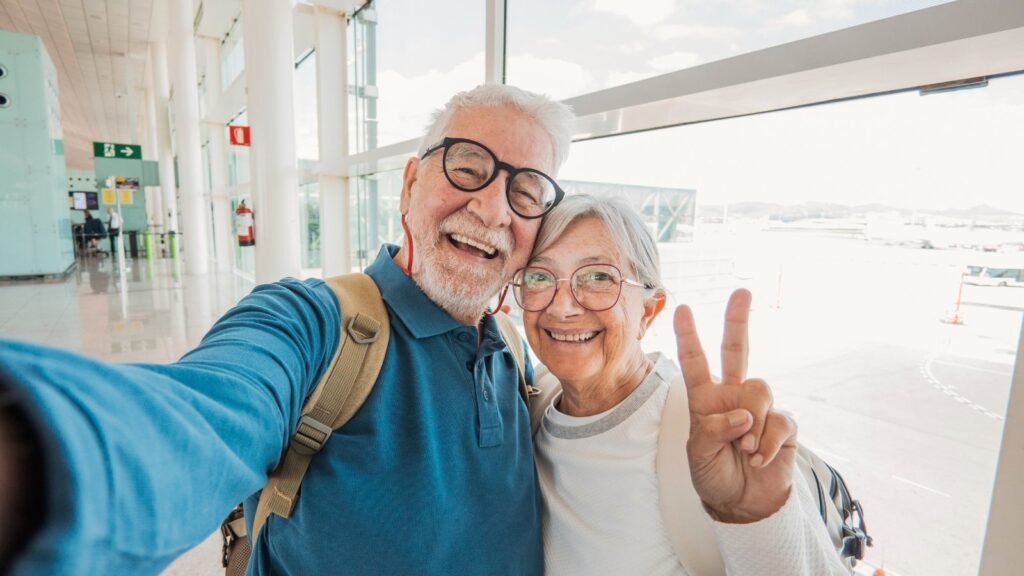 Happy senior couple taking a selfie at an airport terminal, representing the joy and confidence of a seamless luxury Italy trip orchestrated by a Private Italian Concierge.