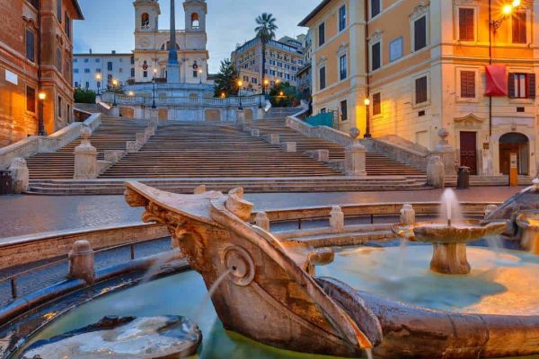 The Spanish Steps illuminated at dusk in Rome, Italy, casting a warm glow on the iconic staircase and its surrounding historic buildings.